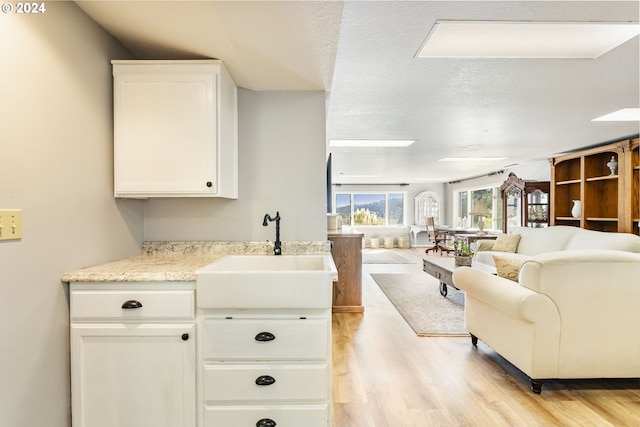 kitchen featuring light wood-style floors, open floor plan, white cabinets, a sink, and a textured ceiling