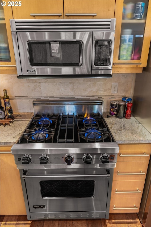 1030 NW Johnson St Unit 323, Portland, OR 97209 - kitchen with appliances with stainless steel finishes, decorative backsplash, glass insert cabinets, and light stone countertops