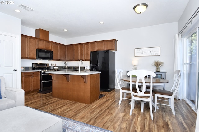 kitchen with sink, a breakfast bar area, a center island with sink, dark hardwood / wood-style flooring, and black appliances