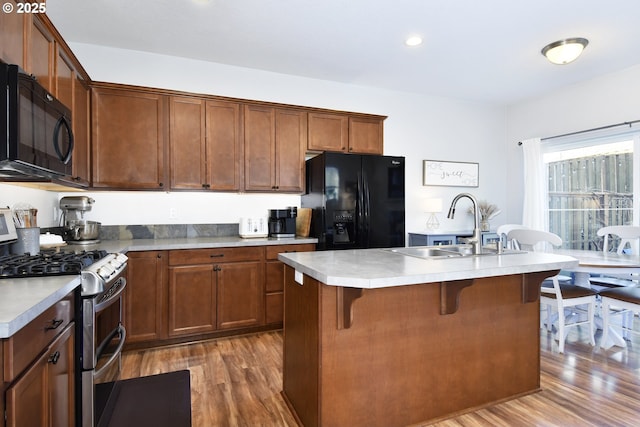 kitchen with sink, a breakfast bar area, an island with sink, hardwood / wood-style flooring, and black appliances