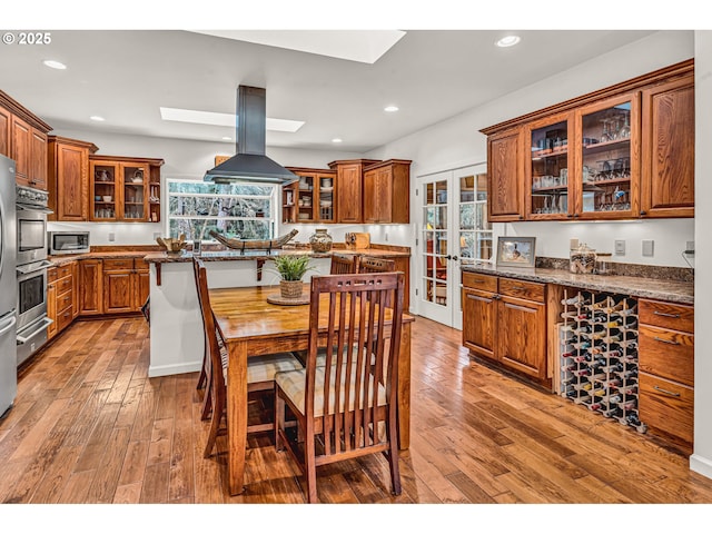 kitchen featuring a skylight, brown cabinetry, island range hood, and light wood finished floors