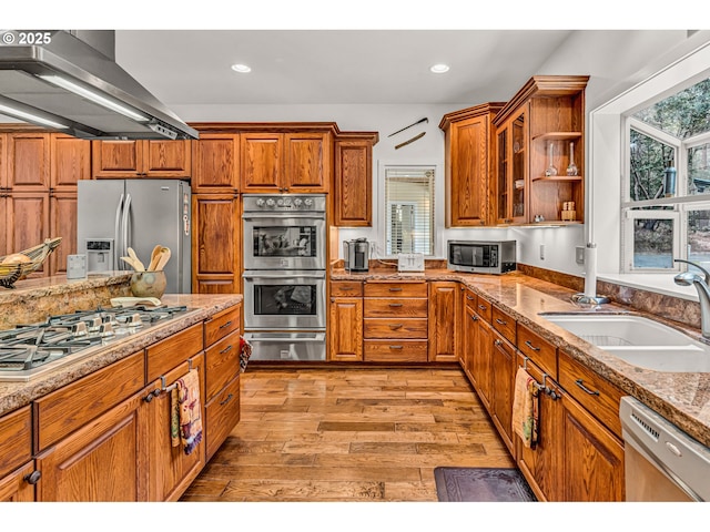kitchen with a sink, light wood-style flooring, stainless steel appliances, under cabinet range hood, and a warming drawer