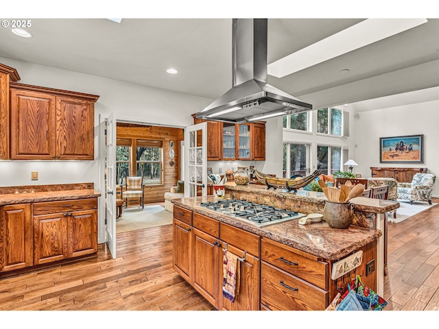 kitchen featuring light wood-style floors, stainless steel gas cooktop, brown cabinetry, open floor plan, and island range hood