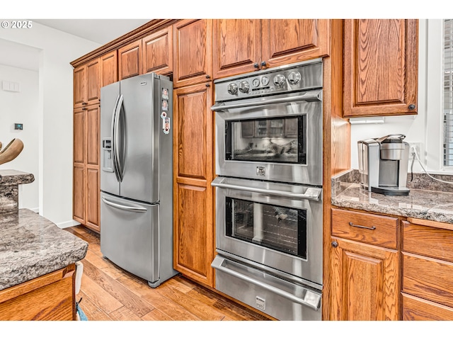 kitchen with appliances with stainless steel finishes, brown cabinets, light wood-type flooring, and a warming drawer