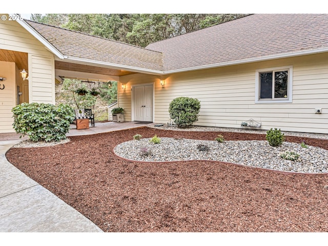 entrance to property with a shingled roof and a patio area