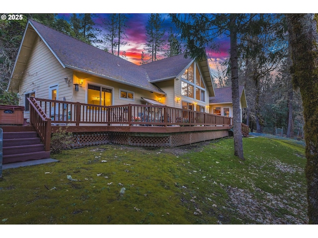 back of house at dusk with a wooden deck and a yard
