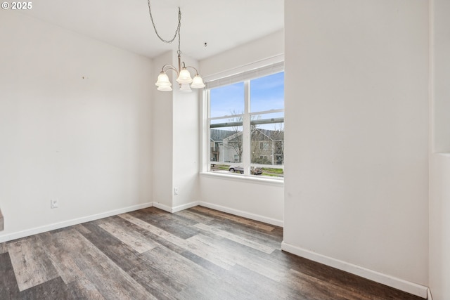 empty room featuring a notable chandelier, wood finished floors, and baseboards