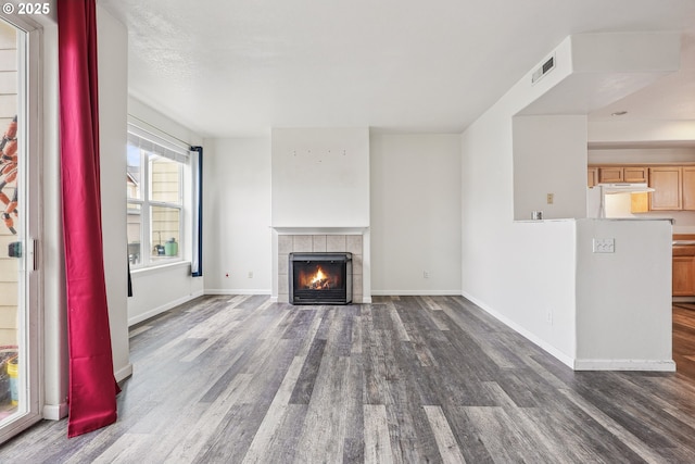 unfurnished living room featuring visible vents, baseboards, dark wood-style floors, and a tiled fireplace