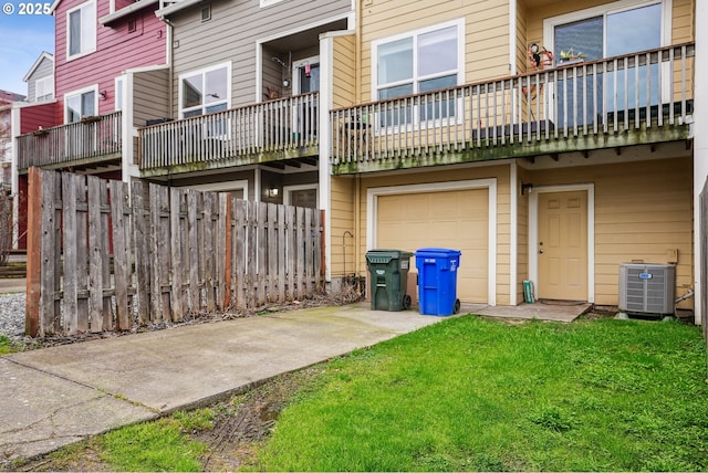 rear view of property featuring fence, concrete driveway, central AC unit, a lawn, and a garage