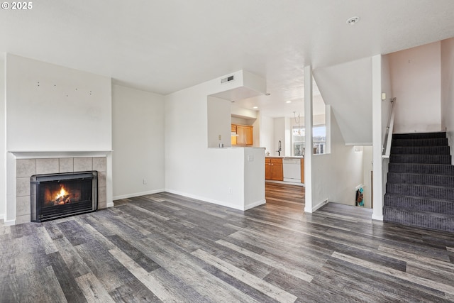 unfurnished living room with a sink, baseboards, a tiled fireplace, stairs, and dark wood-style flooring