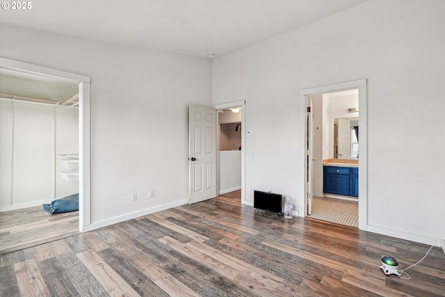 unfurnished bedroom with baseboards, a walk in closet, connected bathroom, and wood finished floors