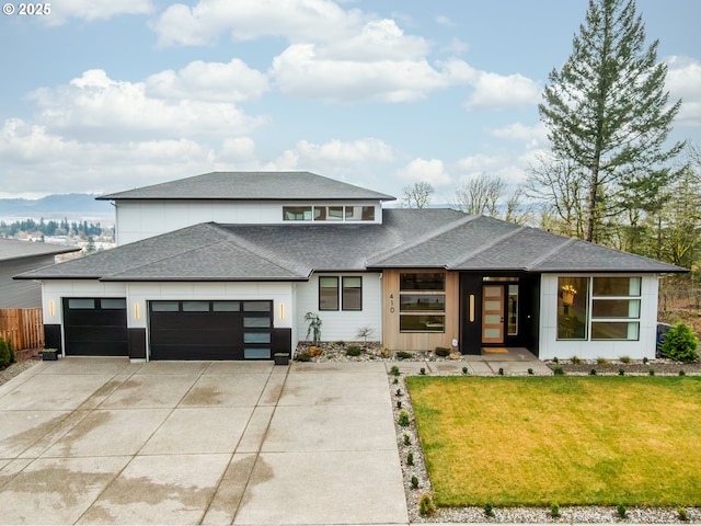 prairie-style house featuring a shingled roof, a front lawn, fence, concrete driveway, and an attached garage