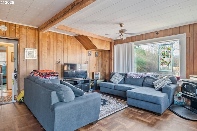 living room featuring ceiling fan, wooden walls, dark parquet flooring, beamed ceiling, and a wood stove