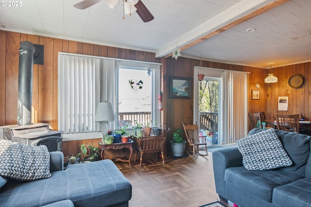 living room featuring wooden walls, dark parquet floors, beamed ceiling, a wood stove, and ceiling fan