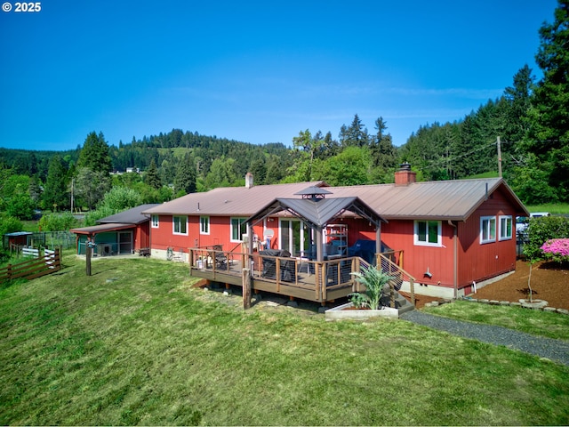 back of property with a yard, a forest view, a wooden deck, and metal roof