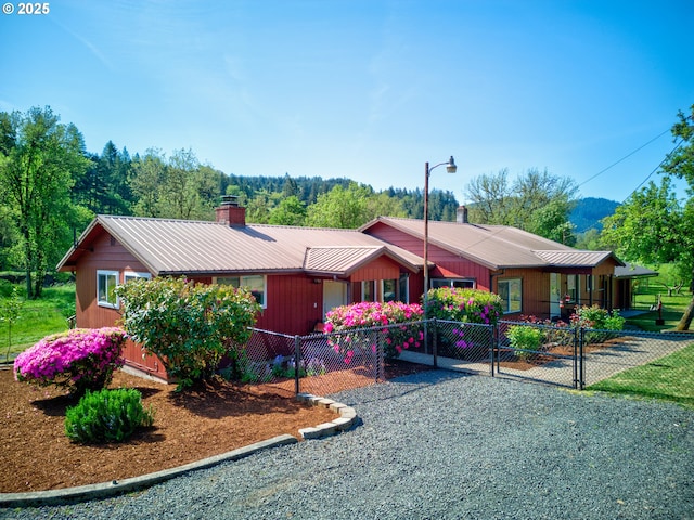 view of front of property featuring a gate, a fenced front yard, a chimney, and metal roof