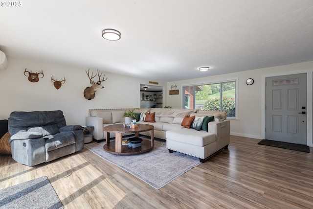 living room with baseboards, a wall unit AC, and wood finished floors