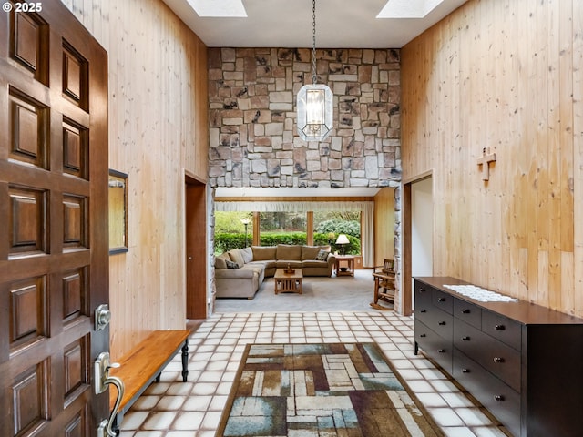 carpeted foyer entrance featuring a towering ceiling, wood walls, and a skylight