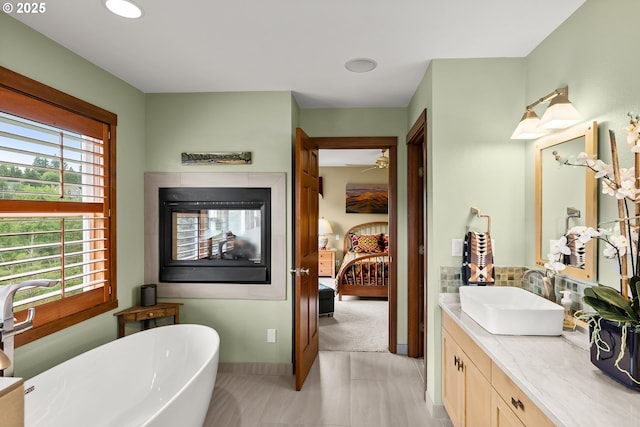 ensuite bathroom with a soaking tub, vanity, ceiling fan, and baseboards