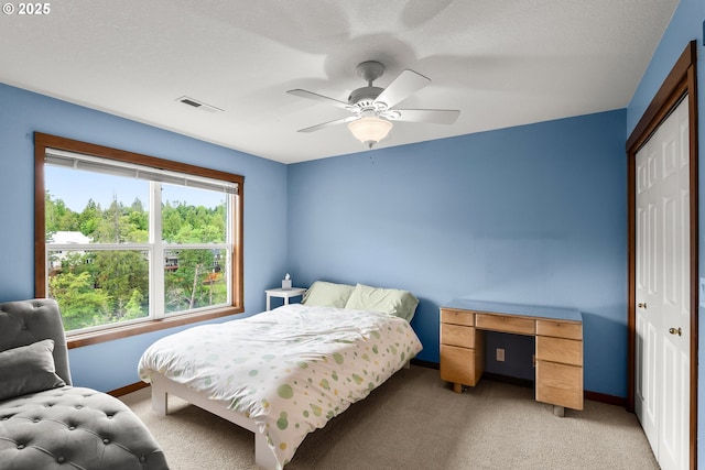 bedroom featuring a closet, light colored carpet, baseboards, and a ceiling fan