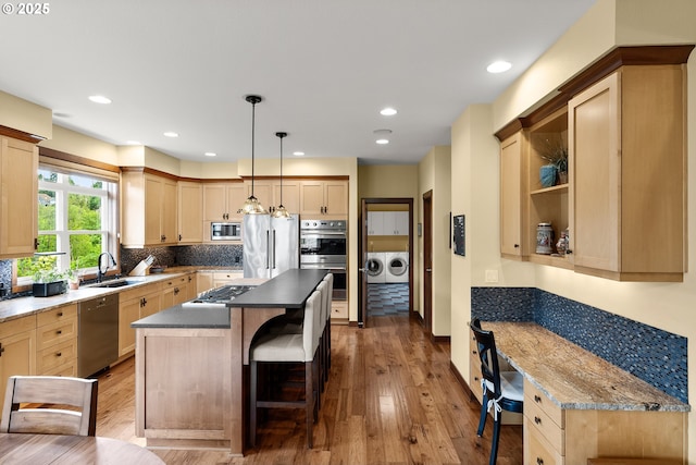 kitchen with stainless steel appliances, washing machine and dryer, a kitchen bar, wood finished floors, and a kitchen island