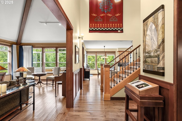 entrance foyer featuring wood finished floors, a towering ceiling, beam ceiling, stairs, and a wainscoted wall