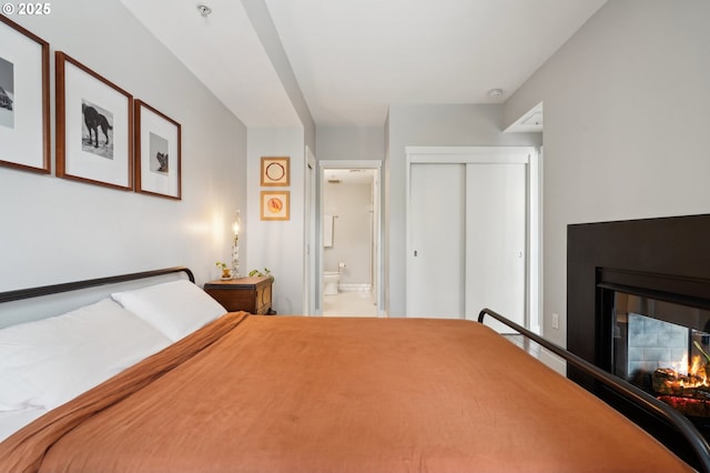 bedroom featuring a closet, a multi sided fireplace, and ensuite bath