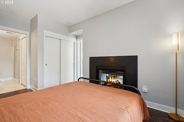 bedroom featuring baseboards, a closet, wood finished floors, and a multi sided fireplace