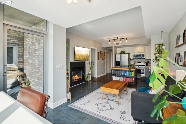 living room featuring track lighting, baseboards, a glass covered fireplace, and finished concrete floors