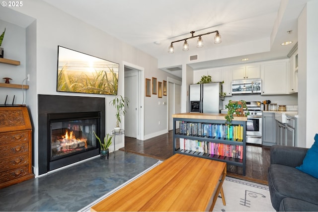 living room with a glass covered fireplace, baseboards, wood finished floors, and visible vents