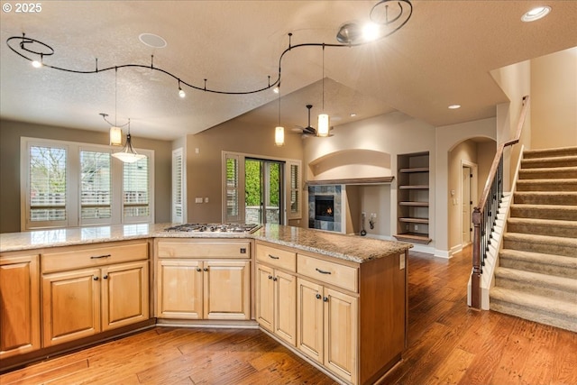 kitchen featuring light wood finished floors, a textured ceiling, light stone counters, and stainless steel gas stovetop