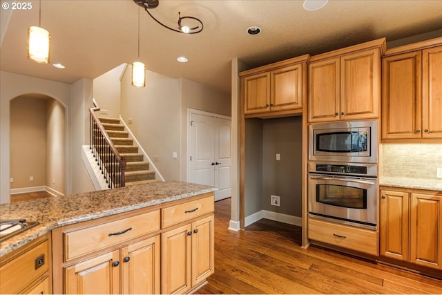 kitchen featuring light stone counters, decorative backsplash, hanging light fixtures, stainless steel appliances, and dark wood-style flooring