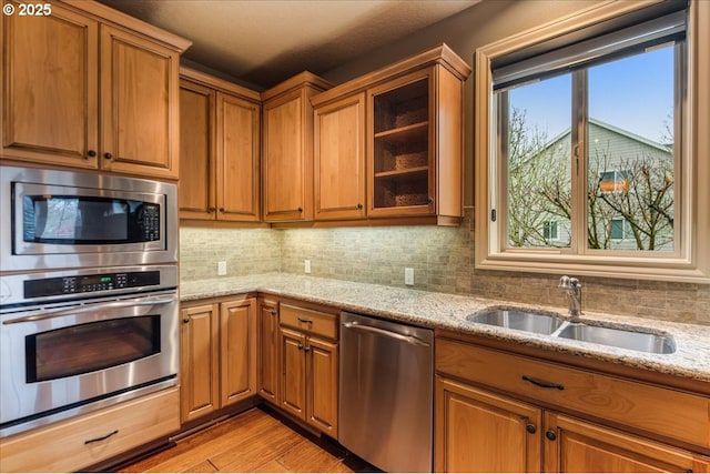 kitchen with a sink, light stone counters, tasteful backsplash, stainless steel appliances, and brown cabinetry