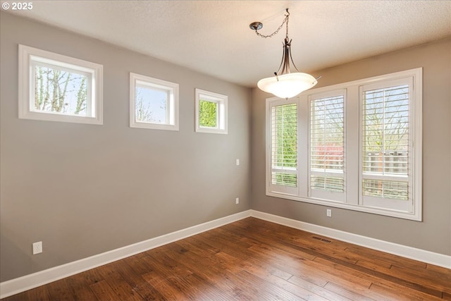 spare room with dark wood finished floors, visible vents, and baseboards