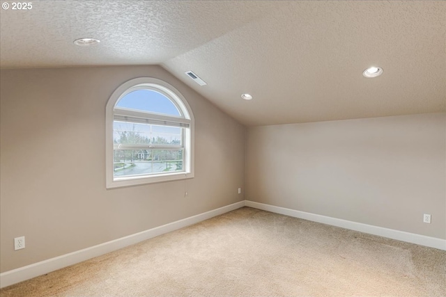 unfurnished room featuring visible vents, lofted ceiling, a textured ceiling, carpet floors, and baseboards