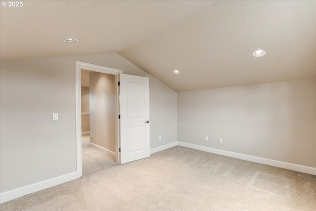 unfurnished room featuring lofted ceiling, baseboards, and light carpet