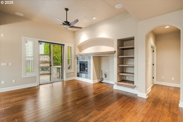 unfurnished living room featuring arched walkways, built in shelves, a ceiling fan, and hardwood / wood-style floors