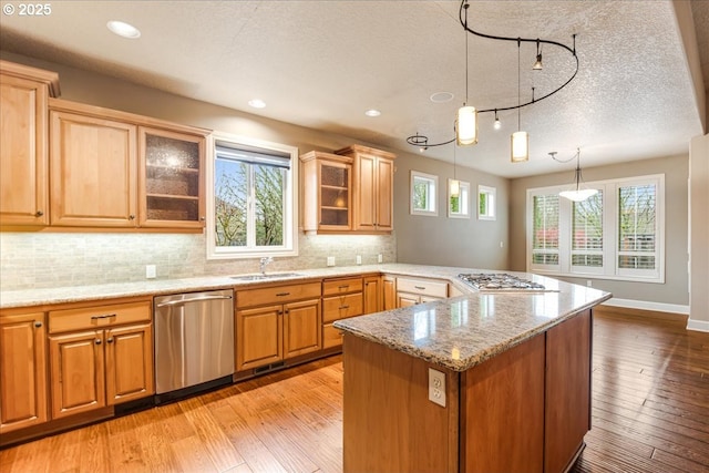 kitchen with a peninsula, light wood-style flooring, appliances with stainless steel finishes, and a sink