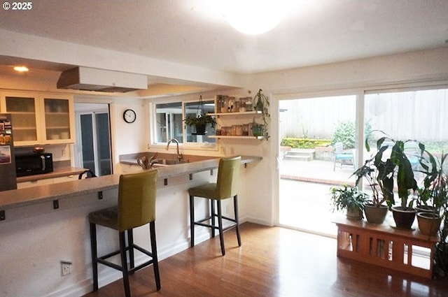 4768 Manzanita St, Eugene, OR 97405 - kitchen featuring a kitchen breakfast bar, wood finished floors, glass insert cabinets, black microwave, and refrigerator