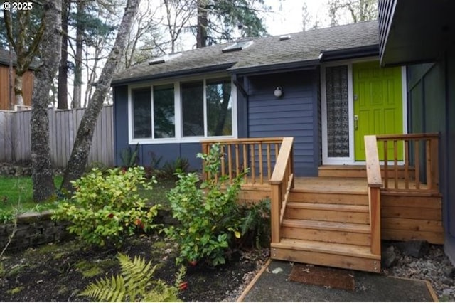 property entrance with fence and roof with shingles