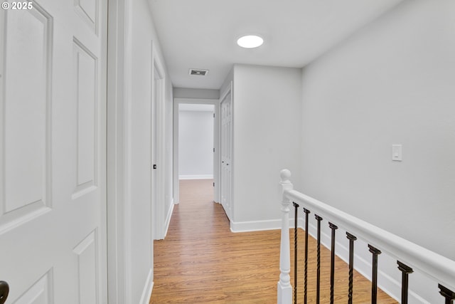 hall with baseboards, visible vents, light wood-type flooring, and an upstairs landing