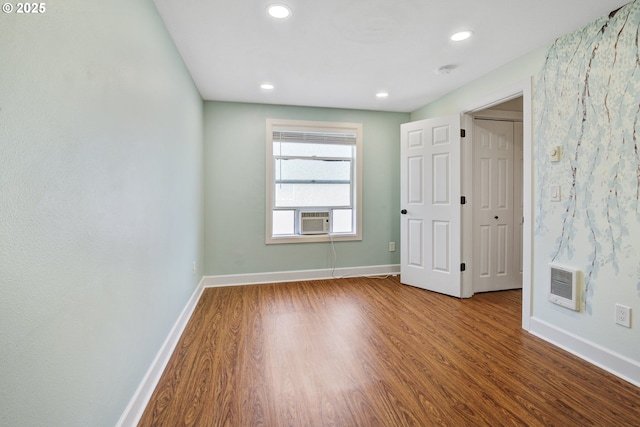 empty room featuring baseboards, heating unit, and wood finished floors