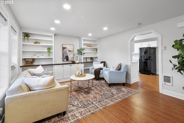 living room with heating unit, wood finished floors, baseboards, recessed lighting, and arched walkways