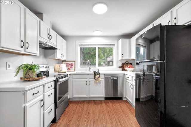 kitchen with appliances with stainless steel finishes, light wood-type flooring, a sink, light countertops, and under cabinet range hood