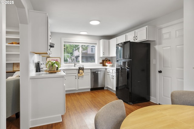 kitchen with a sink, dishwasher, light countertops, freestanding refrigerator, and white cabinetry