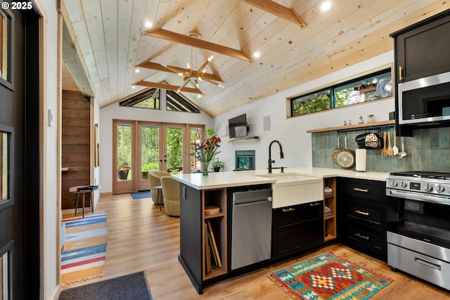kitchen featuring stainless steel appliances, open shelves, a peninsula, light countertops, and a sink