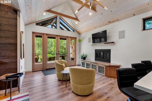 living room featuring light wood finished floors, a glass covered fireplace, a ceiling fan, wooden ceiling, and french doors