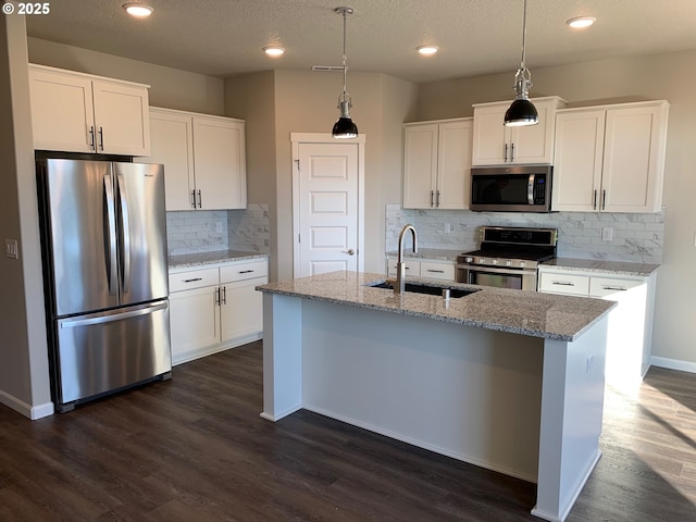 kitchen with appliances with stainless steel finishes, white cabinetry, sink, a kitchen island with sink, and light stone countertops