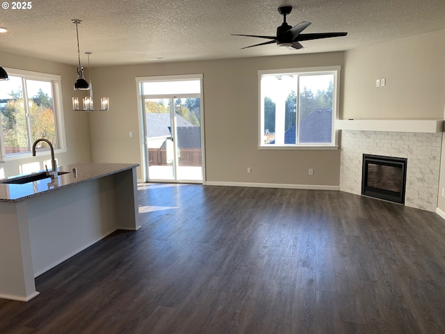 kitchen featuring sink, a brick fireplace, dark hardwood / wood-style flooring, pendant lighting, and light stone countertops