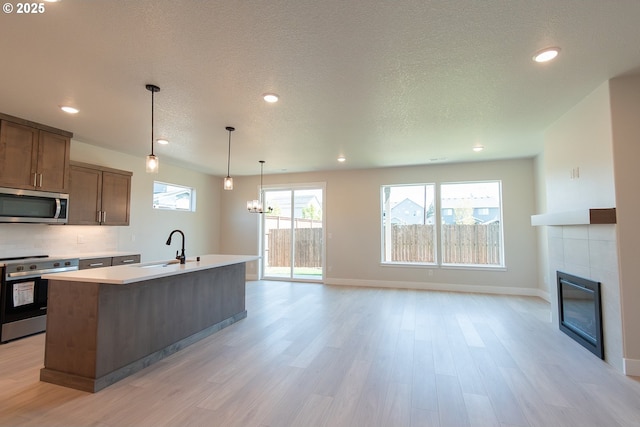 kitchen featuring stainless steel appliances, light countertops, a tile fireplace, light wood finished floors, and an island with sink